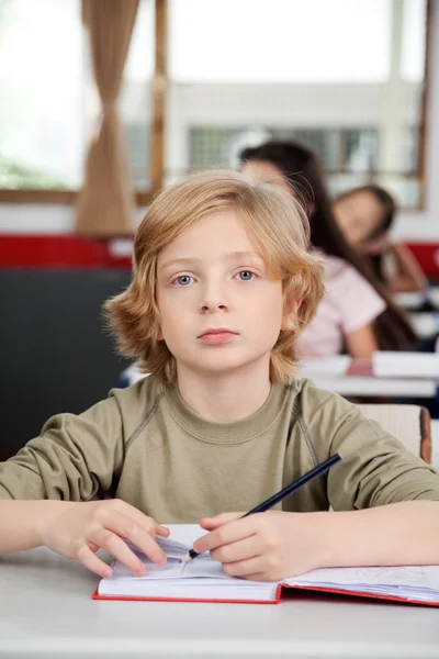 Portrait Of Schoolboy Writing In Book At Desk — Stockfoto