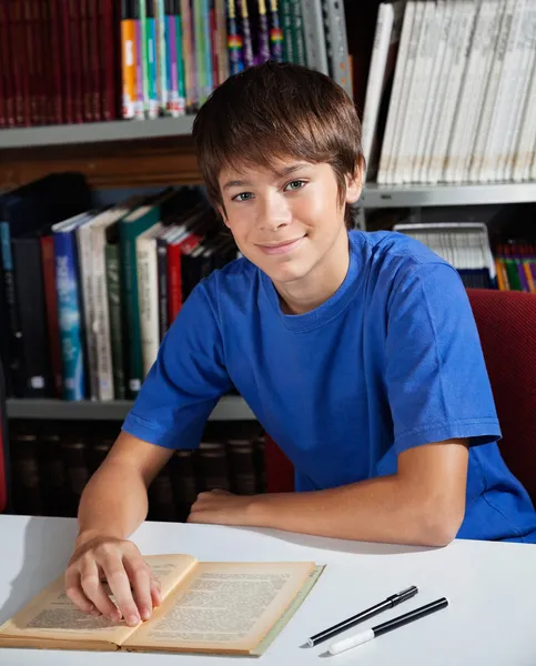 Adolescente estudante sorrindo enquanto sentado na biblioteca — Fotografia de Stock