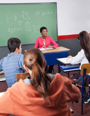 öğretmen ve sınıf içinde oturan genç öğrenciler