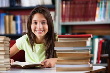 kitaplığındaki kitap yığını ile otururken gülümseyen kız öğrenci