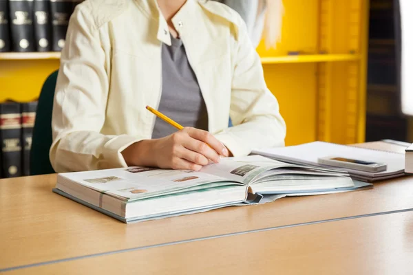 Vrouw met boeken en potlood zitten aan tafel in bibliotheek — Stockfoto