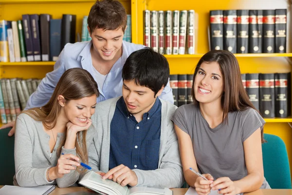 Kvinnlig student med vänner läser bok i biblioteket — Stockfoto