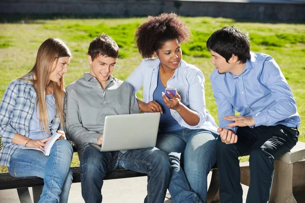 Studenti con computer portatile e cellulare seduto in Campus — Foto Stock