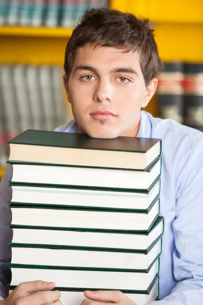 Estudante descansando queixo em livros empilhados na biblioteca — Fotografia de Stock