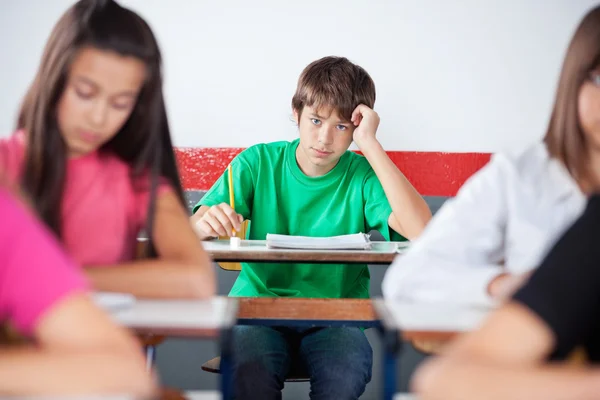 10 代の男子生徒が教室で机の上に傾いた — ストック写真