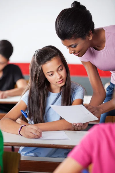 Lehrerin zeigt Studentin am Schreibtisch Papier — Stockfoto