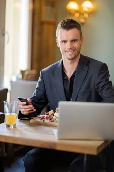 Homem de negócios com celular e laptop no restaurante — Fotografia de Stock