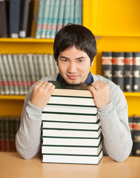 Zelfverzekerde man met gestapelde boeken zit in de bibliotheek van de Universiteit — Stockfoto