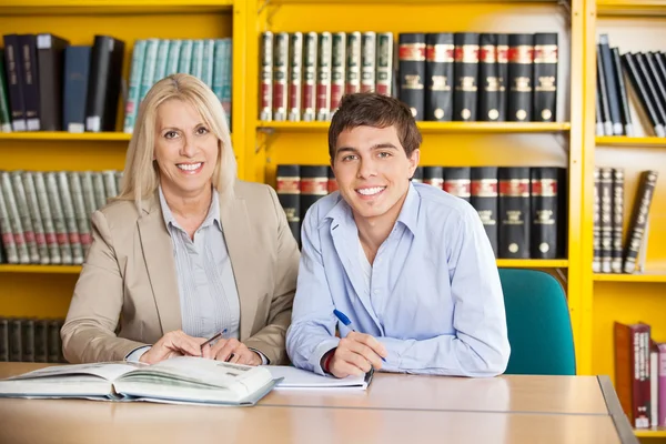 Studente e insegnante con libri seduti a tavola in biblioteca — Foto Stock