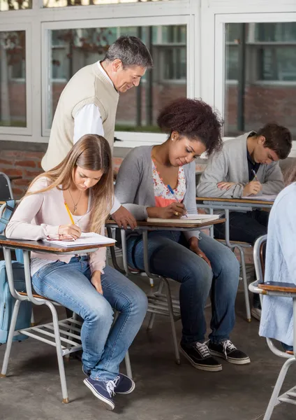 Estudiantes que escriben el examen mientras el profesor los supervisa en clase —  Fotos de Stock