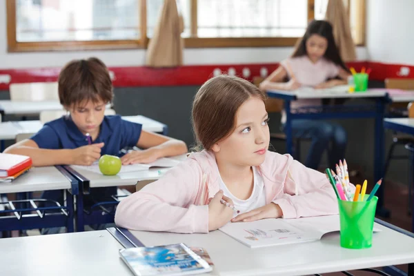 Écolière regardant loin tout en dessinant en salle de classe — Photo