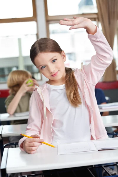Školačka zvyšovat ruku na stůl v učebně — Stock fotografie