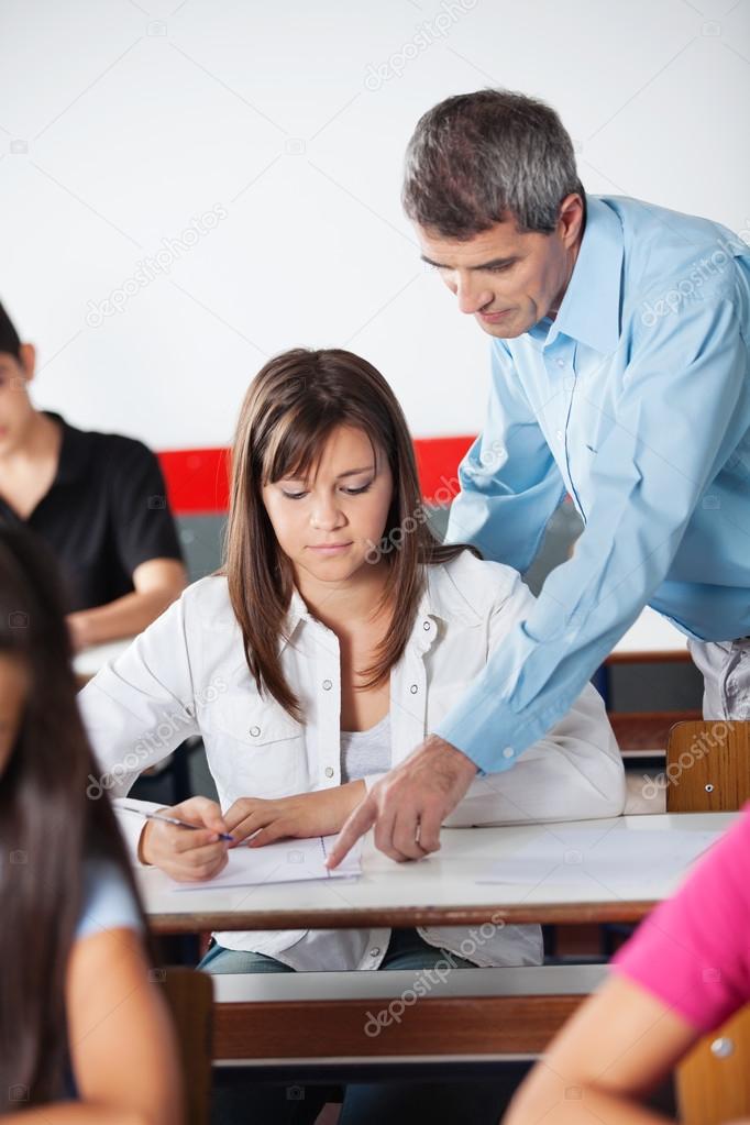 Male Teacher Assisting Female Student At Desk