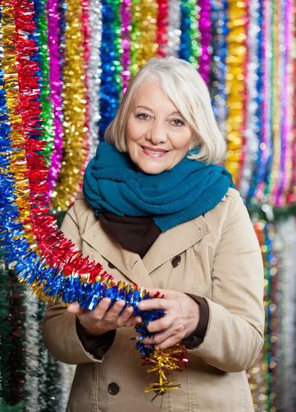 Senior Woman Holding Tinsels At Christmas Store — Stock Photo, Image