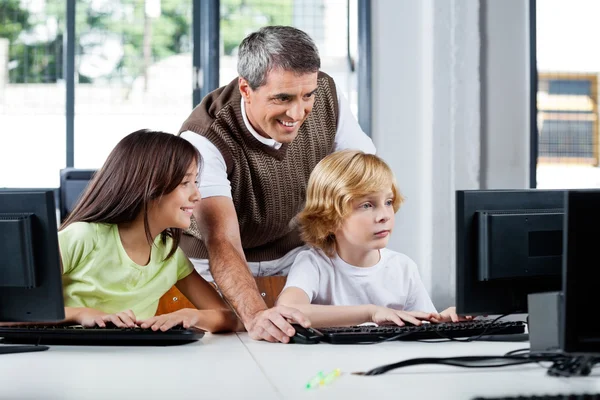 Glad lärare hjälpa skolbarn med stationär pc — Stockfoto