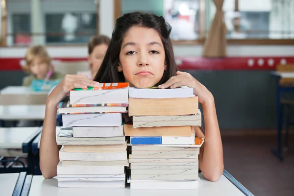 Сумна школярка відпочиває на складених книгах на робочому столі — стокове фото