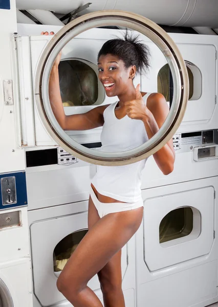 Kvinna gestikulerande tummen upp stående av torktumlare i tvätt — Stockfoto