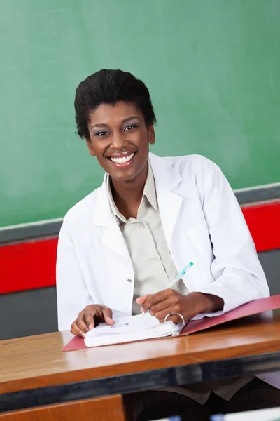 Happy Teacher With Pen And Binder Sitting At Desk — Stock Photo, Image