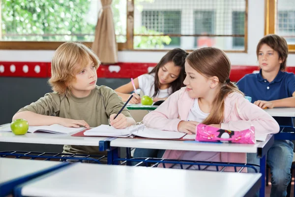 Školák při pohledu na dívku při psaní na stůl — Stock fotografie