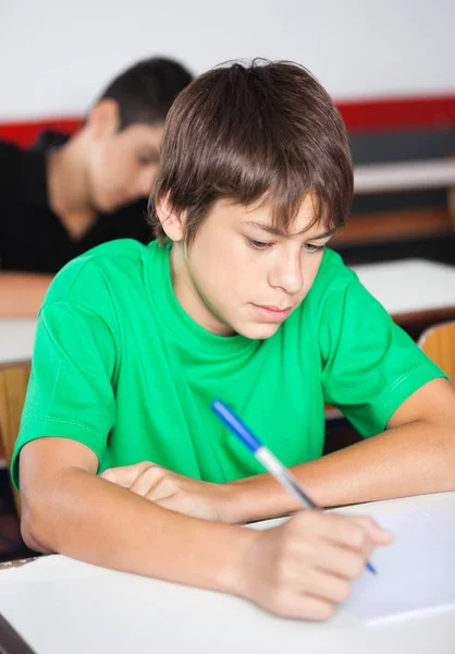 Teenage skolpojke skriva på skrivbord under granskningen — Stockfoto