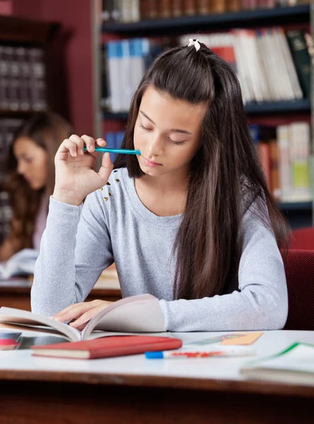 Estudante segurando caneta enquanto lia livro na biblioteca — Fotografia de Stock