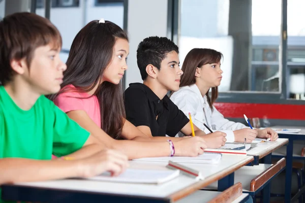 Estudiantes adolescentes mirando hacia otro lado mientras estudian en el escritorio —  Fotos de Stock