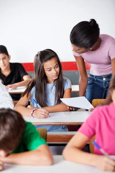 Kadın öğretmen masasındaki kız öğrenci için kağıt gösteriliyor — Stok fotoğraf