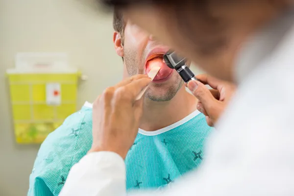 Docteur avec dépresseur et otoscope examinant la langue du patient — Photo