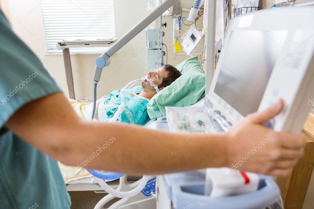 Nurse Pressing Monitor's Button With Patient Lying On Bed