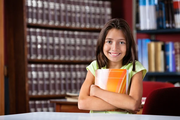 Söt skolflicka håller boken sitter i biblioteket — Stockfoto