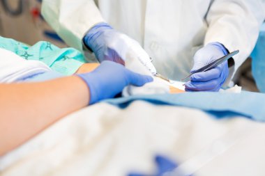 Doctor Stitching Patient's Wound While Nurse Assisting Him clipart
