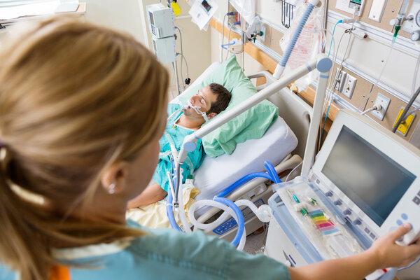 Nurse Pressing Monitor's Button With Patient Lying On Bed