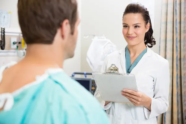 Arzt mit Klemmbrett lächelt Patientin an — Stockfoto