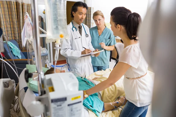 Donna in piedi vicino al letto del paziente guardando medico e infermiera — Foto Stock