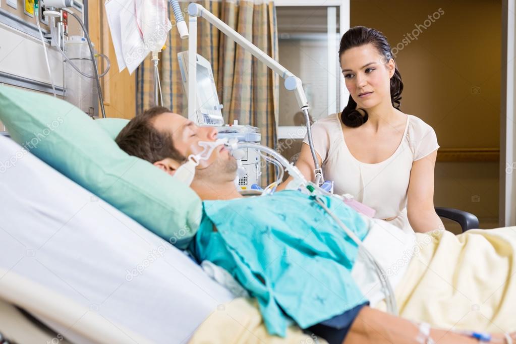 Woman Looking At Critical Patient Lying On Bed