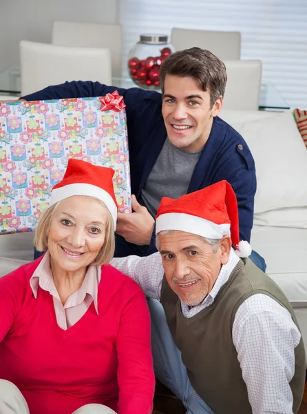 Rodina s vánoční současné usmívající se doma — Stock fotografie