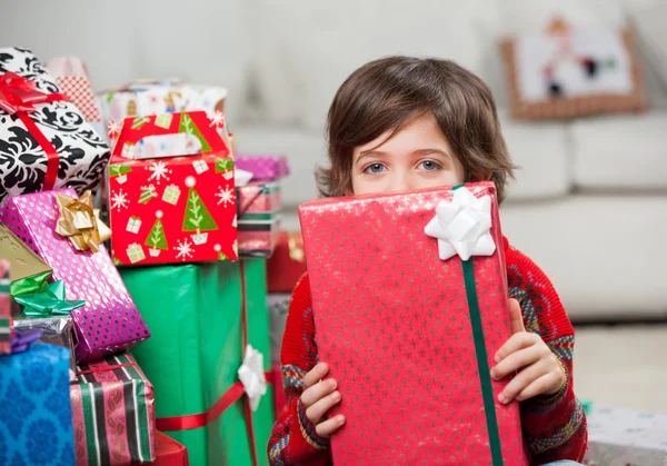 Menino segurando presente de Natal na frente da cara — Fotografia de Stock