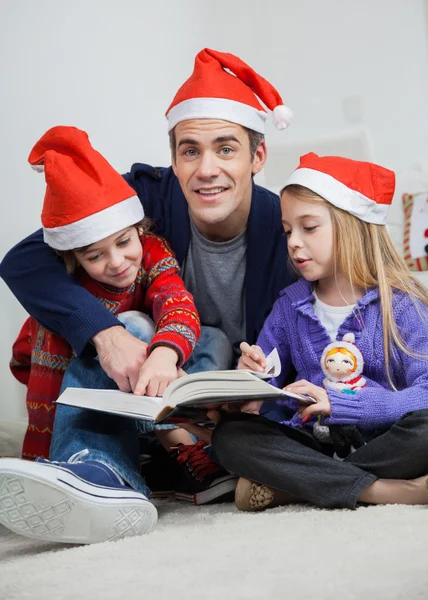Ojciec z dziećmi czytanie książki podczas świąt Bożego Narodzenia — Zdjęcie stockowe