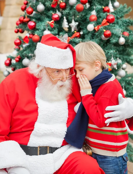 Niño diciendo deseo en el oído de Santa Claus —  Fotos de Stock