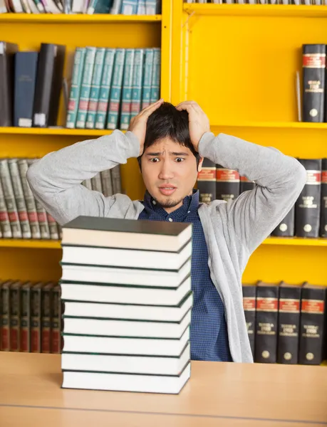 Homem confuso olhando livros empilhados na biblioteca — Fotografia de Stock