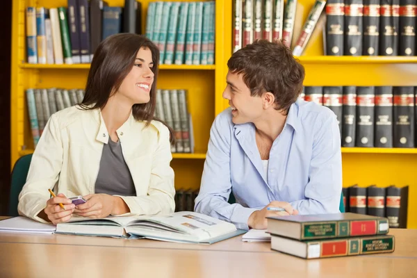Friends Looking At Each Other Against Bookshelf In Library — Stock Photo, Image