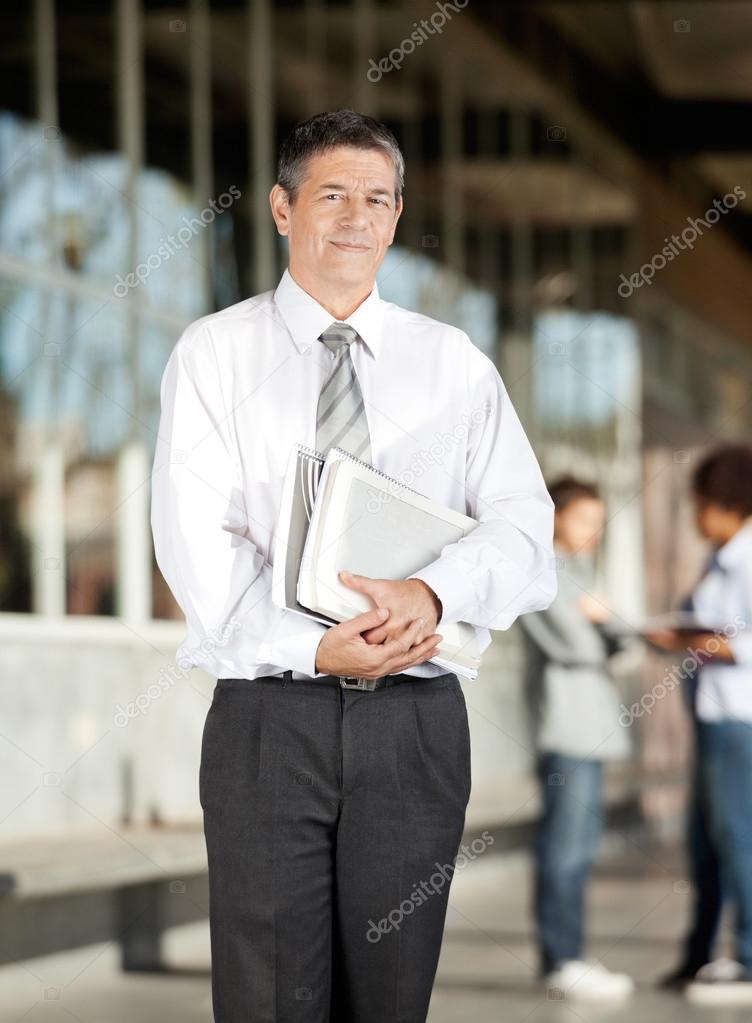 Professor With Book Standing On University Campus