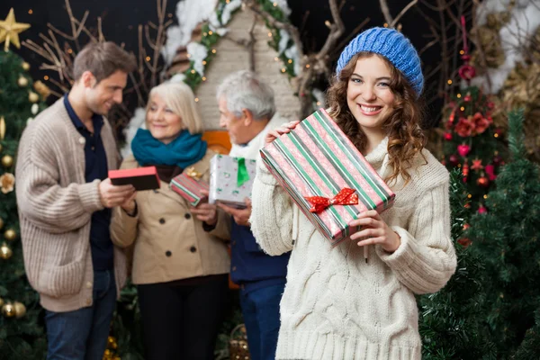 Žena držící vánoční dárek s rodinou v pozadí — Stock fotografie