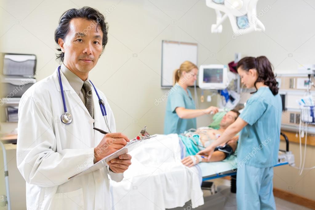 Doctor Holding Clipboard With Nurses Examining Patient