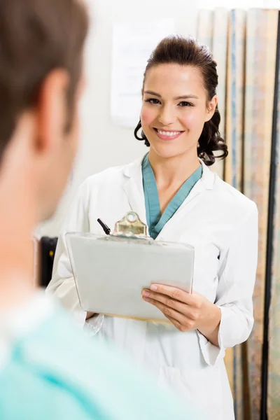 Doctor con portapapeles de pie por paciente — Foto de Stock