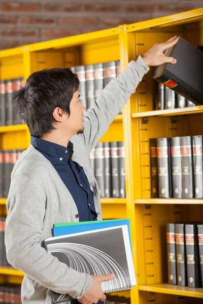 Student Taking Book From Shelf In University Library