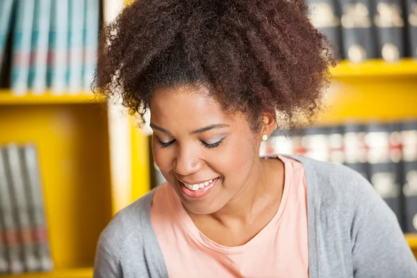 Student glimlachend tegen boekenplank in bibliotheek — Stockfoto