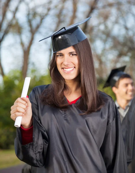 Mujer en vestido de graduación con diploma en el campus universitario —  Fotos de Stock