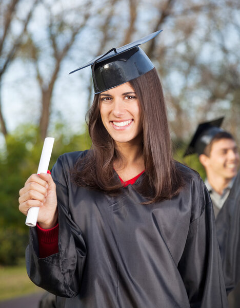 Woman In Graduation Gown Holding Diploma On College Campus