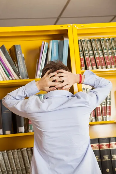 Frustrado hombre de pie contra librería en la biblioteca —  Fotos de Stock